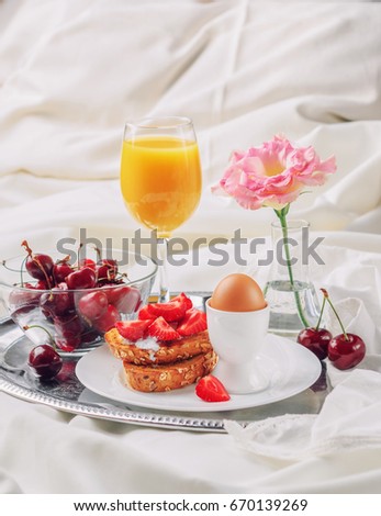 Summer breakfast in bed: toast of unleavened bread, homemade yogurt, fresh organic strawberry, sweet cherry, soft-boiled egg, a glass of fresh orange juice on a metal tray on a light background