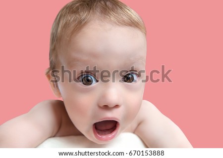 Close up of very surprised, shocked baby boy with open mouth and big eyes looking at viewer, pink background