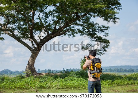 Man with backpack standing in front of tree and taking a photo.