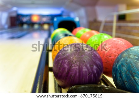Bowling room with the colorful bowling balls in return machine. Old bowling balls on the rack for background. Selective focus.