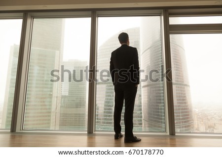 Contemplative businessman standing near big window looking out at city, thoughtful entrepreneur building future plans, thinking over ways to overcome business problems, pass through crisis, back view  Royalty-Free Stock Photo #670178770
