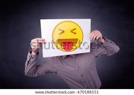 Young businessman hiding behind a playful emoticon on cardboard 