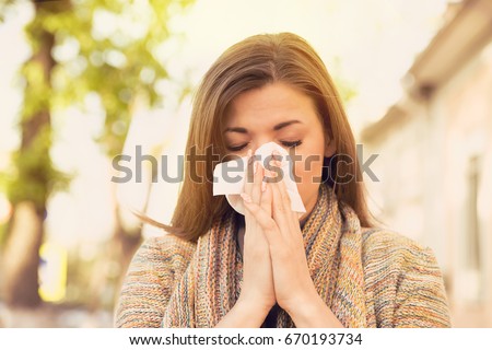 Woman with allergy symptoms blowing nose Royalty-Free Stock Photo #670193734