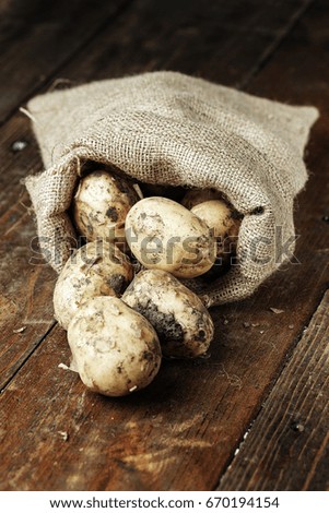lot of young potatoes in a sackcloth sack on a wooden background