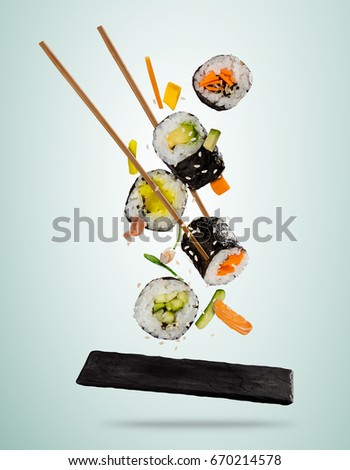 Flying sushi pieces served on stone plate, separated on soft background. Many kinds of popular sushi food with chopsticks. Very high resolution image
