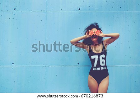 Active slim girl having fun enjoying outdoors sports activities carrying about healthy nutrition and lifestyle while standing with grape fruit on blue wall copy space background for advertise content