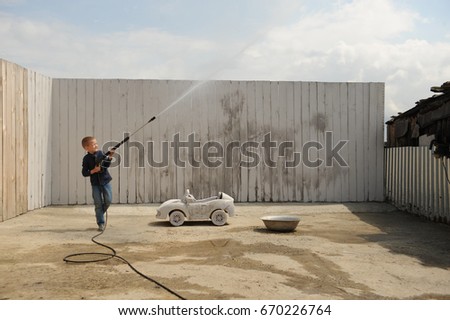 A young dude plays with a car wash hose and a race prize in a rural compound in a hot summer