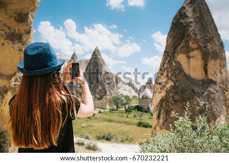 A tourist girl makes a photo on the phone in memory of a beautiful view of the hills in Cappadocia in Turkey. Travel, tourism, hiking, vacation.