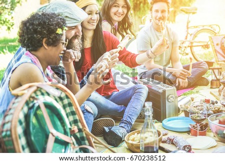 Happy friends eating and drinking at picnic dinner on nature - Young diverse culture people having fun at pic-nic bbq sitting on grass - Focus on center girl - Youth,food and friendship concept