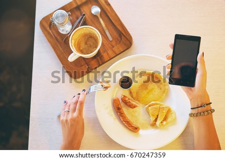 Close up of women's hands holding smartphone with blank copy space screen. Watching video on mobile phone during breakfast.