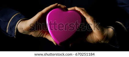Black Mania. female hands isolated on black background showing heart shaped candy box