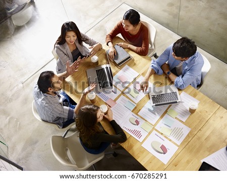 high angle view of a team of asian and caucasian corporate executives discussing business in meeting room.