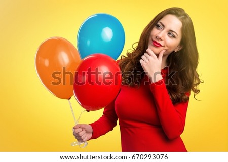 Beautiful young girl holding balloons and thinking on colorful background