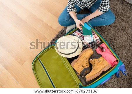 high angle view photo of young woman sitting on living room floor packing luggage showing boarding card and passport with credit card.