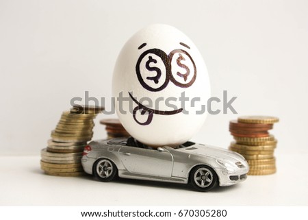 Business concept. Business car. An egg with a painted face and a sticky tongue in the middle of a pile of coins. Egg on a gray car. Photo for your design
