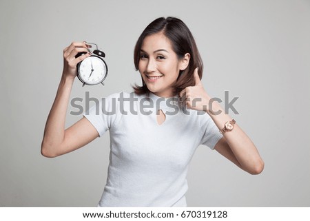 Young Asian woman show thumbs up with a clock on gray background