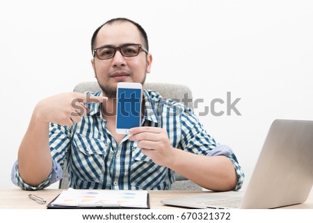 Portrait of businessman sitting behind table showing smartphone with blue screen isolated on white background.
