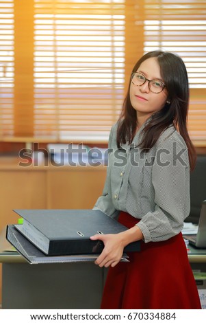 Portrait of pretty lovely bright young business woman on workplace standing holding a office document folders with documents and with and other supplies.