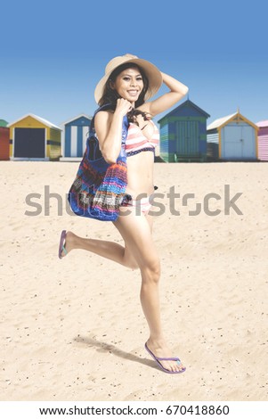 Picture of a beautiful woman wearing swimsuit while carrying a handbag and running near the cottage