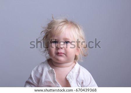 beautiful child with white hair. Portrait of chubby child, long fluffy blonde hair, blue eyes, dressed in a white robe sitting on a Gray background.