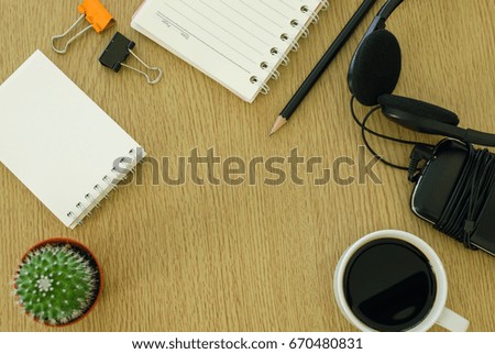Top view of paper note,pencil,black coffee,head phones,mobile phone and cactus on wooden table,this image for business concept.