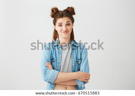 Portrait of displeased young girl with buns looking at camera over white background. Crossed arms.