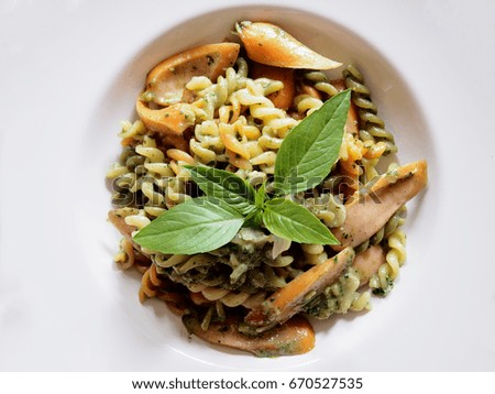 Top view picture of fusilli pesto sauce with sausage on white plate above wooden table.