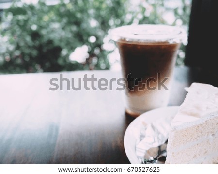 The picture of coconut cake and iced caramel macchiato on wooden table near the window.  selective focus