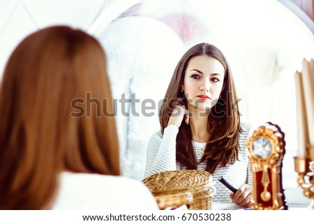 Close up of beautiful pleasant delighted girl sitting in front of the mirror and looking straight while feeling content