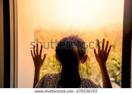 Sad little girl in room and looking out the window Royalty-Free Stock Photo #670536592