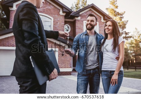 Happy couple is taking keys from their new house from broker and smiling. Royalty-Free Stock Photo #670537618