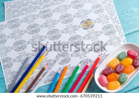 White sheet of paper, coloring for adults for rest and relaxation. Blue vintage background, painted wood. Colour pencils. colored candies in the saucer.