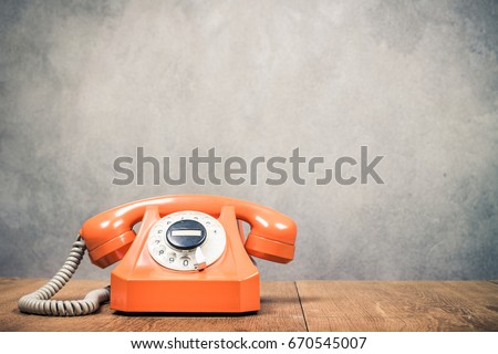 Old orange retro rotary telephone from 60s on table front textured concrete wall background. Vintage style filtered photo