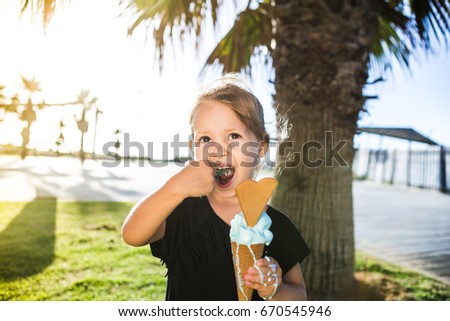 A beautiful baby girl in a black dress on a sunset with ice cream.