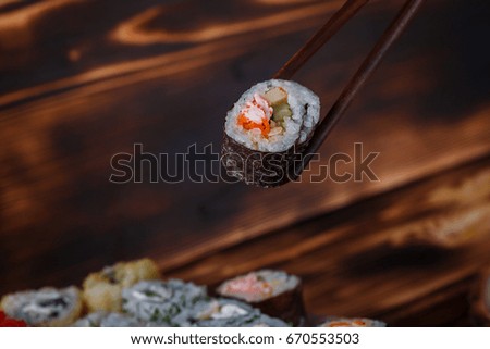 close up of chopsticks taking portion of sushi roll on the table restaurant / eating sushi roll using chopsticks
