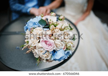 Young gorgeous wedding couple sitting by the glass table with a bouquet.
