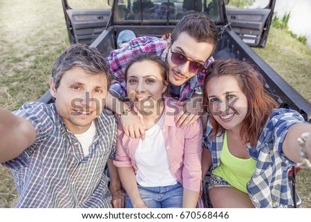Happy group of young friends toasting with beer and takes a selfie outdoors at sunset