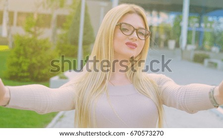 Selfie portrait of a beautiful girl in a beige dress and glasses during the day outdoors. The model is posing in front of the camera. The concept of a beautiful life.