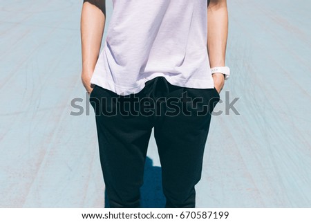 Cropped image of woman in sports pants and t-shirt is standing with hands in pockets, close-up