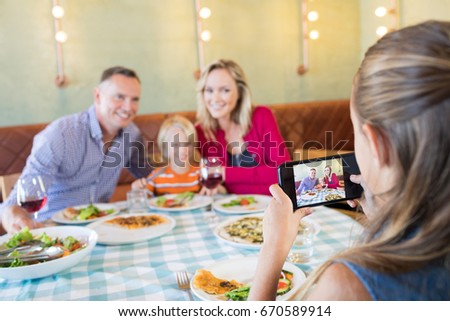 Girl photographing family through mobile phone at restaurant