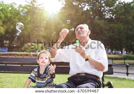 grandfather blowing soap bubbles to his grandchild Royalty-Free Stock Photo #670599487