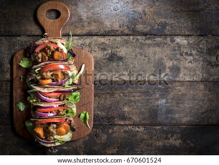 Mini tortilla sandwiches with ground meat and vegetables salad on wooden background with blank space 
