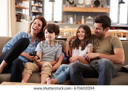 Family Sitting On Sofa In Open Plan Lounge Watching Television Royalty-Free Stock Photo #670602004
