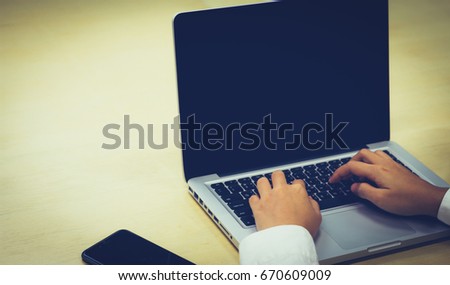 Businessman's hands using laptop on wooden table at office.