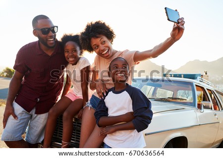 Family Posing For Selfie Next To Car Packed For Road Trip