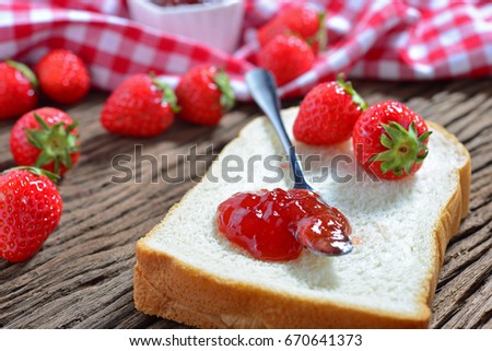 Closeup of strawberry jam on the butter knife with fresh strawberry and bread on wooden table. Selective focus for designed works. Homemade delicious strawberry jam.