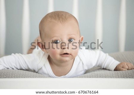 Cute baby caucasian boy lying on a soft blanket in a white crib.