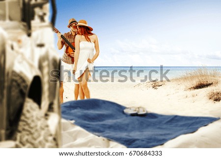 Photo of summer beach with two lovers on sand and blurred big car with towel 