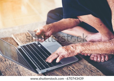 Old senior woman using laptop and hand holding credit card shopping internet on wooden background ,Thailand