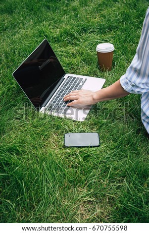close up view of woman sitting on grass and typing on laptop
